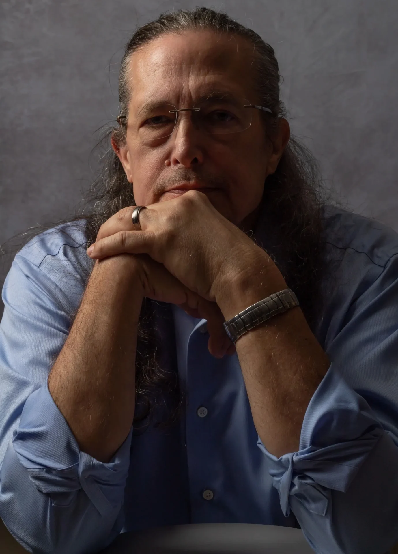 A man with long hair and glasses is sitting down